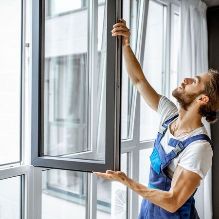 Arbeiter in Latzhose beim Einbau oder der Reparatur eines Fensters.
